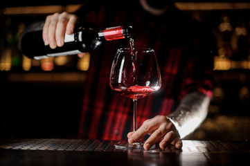 Fototapeta na wymiar Tattooed barman pouring red wine into the burgunya glass