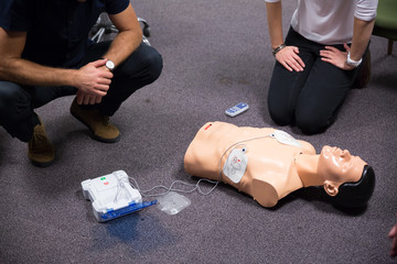 CPR training medical procedure workshop. Demonstrating chest compressions and use of AED automatic defibrillator on CPR doll.