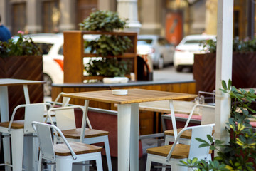 Empty table in the summer terrace cafe, a wooden tabletop and an iron leg against the background of chairs and shelves with plants.