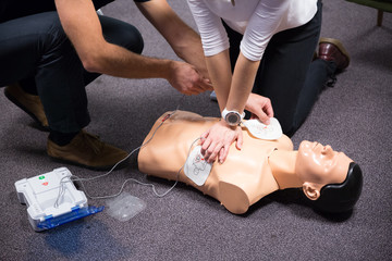 CPR training medical procedure workshop. Demonstrating chest compressions and use of AED automatic defibrillator on CPR doll. - obrazy, fototapety, plakaty