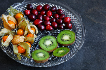 Physalis fruit - Cape gooseberries with cranberries and kiwi on cut glass platter on slate background - with copy space