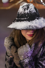 Young girl standing in front of christmas tree lights at night with snowflakes falling, snowing