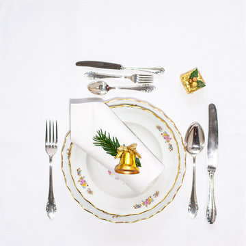 Christmas dinner set: porcelain plates, silver cutery and white napking lying via diagonal line with christmas decoration. Flatlay. Copy space.
