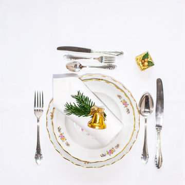Christmas dinner set: porcelain plates, silver cutery and white napking lying via diagonal line with christmas decoration. Flatlay. Copy space.
