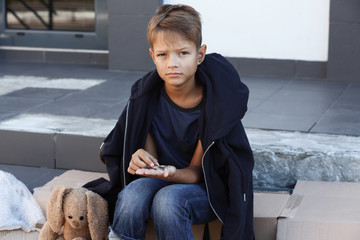 Poor little boy counting coins on city street