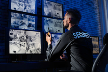Male security guard with portable transmitter monitoring modern CCTV cameras indoors