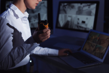 Female security guard with portable transmitter monitoring home cameras indoors at night, closeup