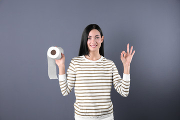 Beautiful woman holding toilet paper roll on color background