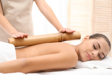 Young woman having massage with bamboo stick in wellness center