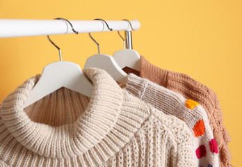 Collection of warm sweaters hanging on rack against color background, closeup