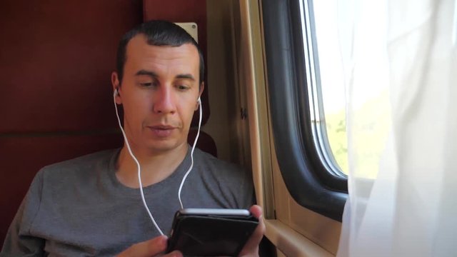 man listening to the music on the train rail car coupe compartment travel. slow motion video. man lifestyle with a smartphone at the window of a train in a car travel internet social media web. man