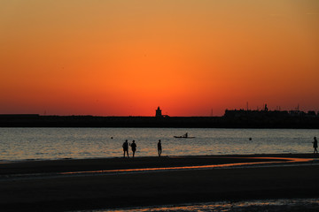 Naklejka na ściany i meble People walking at the beach against sunset