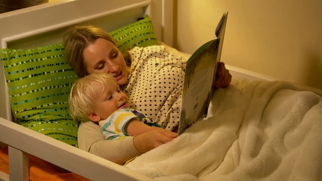 mother and baby son reading a book in bed