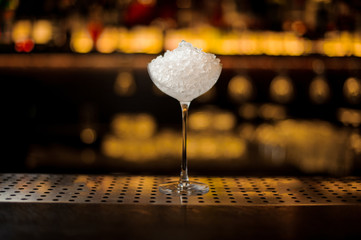 Cocktail glass full of crushed ice standing on the bar counter