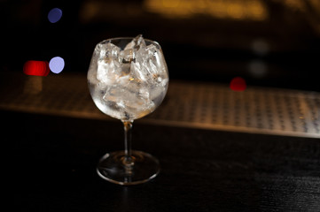 Gin Tonic cocktail glass full of ice cubes standing on the bar counter