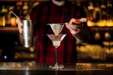 Bartender holding a steeel cocktail shaker and sieve above the glass