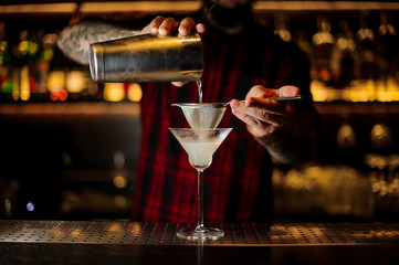 Bartender pourring a White Lady cocktail from the steel shaker