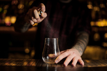 Bartender spraying on a empty cocktail glass in the bar