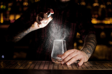 Bartender spraying on the empty cocktail glass in the bar