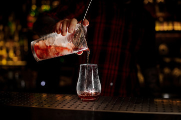 Bartender pourring a Sazerac cocktail from the measuring cup