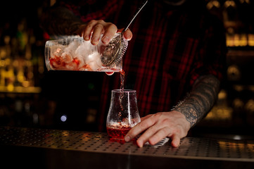 Bartender pourring a Sazerac cocktail from the glass measuring cup