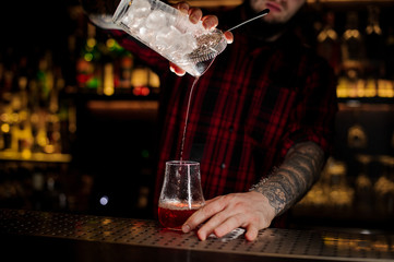 Bartender pourring a Sazerac cocktail from the measuring cup with ice