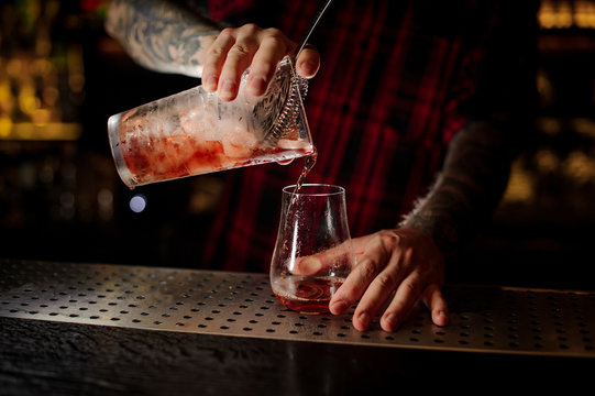 Bartender pourring a red tasty Sazerac cocktail from the measuring cup