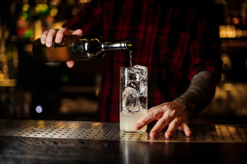 Bartender pourring a achohol from the bottle making cocktail drink