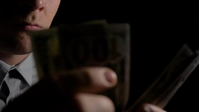 A man in the dark counting dollars. The man counts the dollars. Money in men's hands. Unexpected win. The fee for the work done.He shakes with money. Close up. Slow motion. 4K