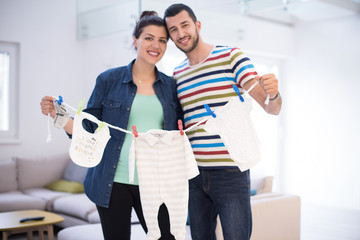 young couple holding baby bodysuits at home