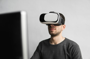 Young man wearing virtual reality goggles headset, vr box and sitting in the office against computer monitor. Connection, technology, new generation, progress concept.