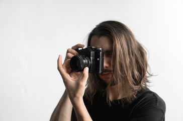 Handsome young bearded man with a long hair and in a black shirt holding vintage old-fashioned film...