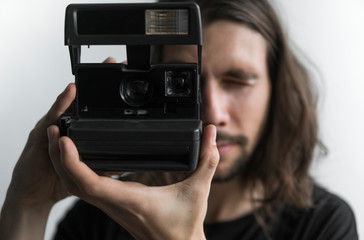 Handsome young bearded man with a long hair and in a black shirt holding vintage old-fashioned film...