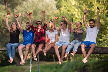 friends enjoying watermelon while sitting on the wooden bridge