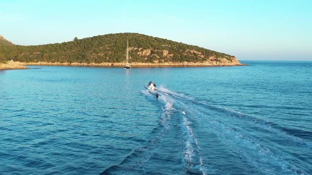 Video from above, aerial view of a person who is doing water skiing at sunset. Sardinia, Italy.