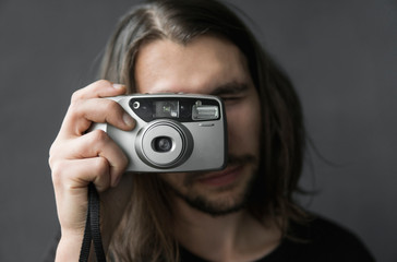 Handsome young bearded man with a long hair and in a black shirt holding vintage old-fashioned film...