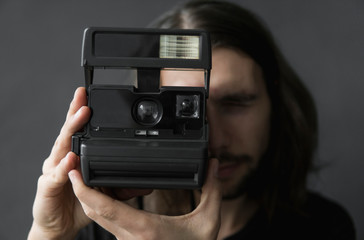 Handsome young bearded man with a long hair and in a black shirt holding vintage old-fashioned film...
