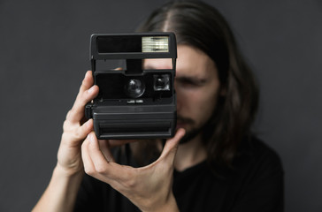 Handsome young bearded man with a long hair and in a black shirt holding vintage old-fashioned film...