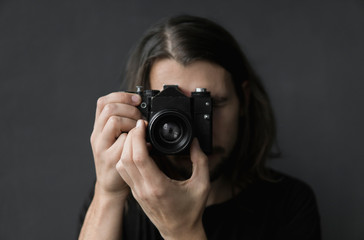 Handsome young bearded man with a long hair and in a black shirt holding vintage old-fashioned film...