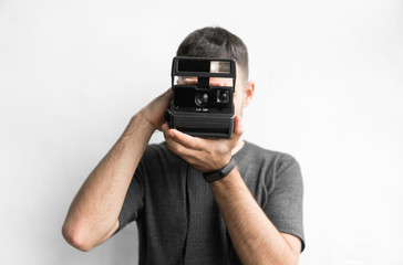 Handsome young bearded man in a black shirt holding vintage old-fashioned film camera on a white...