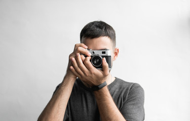 Handsome young bearded man in a black shirt holding vintage old-fashioned film camera on a white...