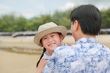 Happy little Asian child girl with his father carries on the beach.