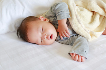 Peaceful newborn Asian baby boy sleeping on bed with the blanket.