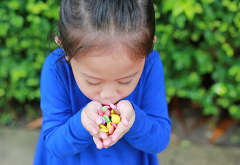 Close-up little Asian child girl holding some colored coated chocolate candy in her hands.