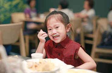 Adorable little asian girl at restaurant having breakfast
