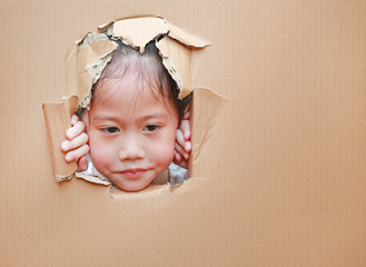 Adorable little Asian child girl looking through hole on cardboard.