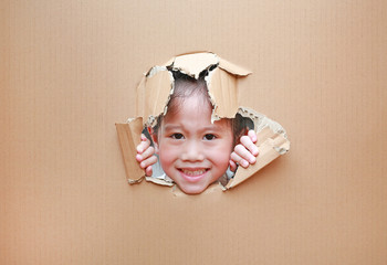Happy Asian kid girl looking through hole on cardboard with copy space.