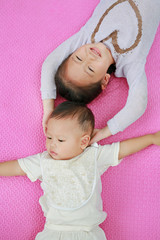 Adorable cute Asian sister and little brother lying on pink mattress mat looking at camera. View from above.