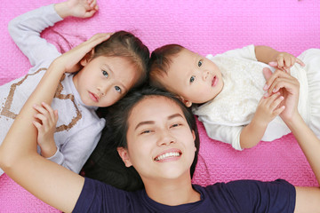 Happy Young Asian mother daughter and son lying on pink mattress mat looking at camera. View from above.