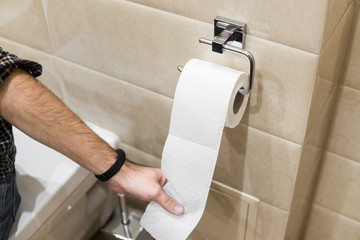 Close-up roll toilet paper in restroom with hand pulling.